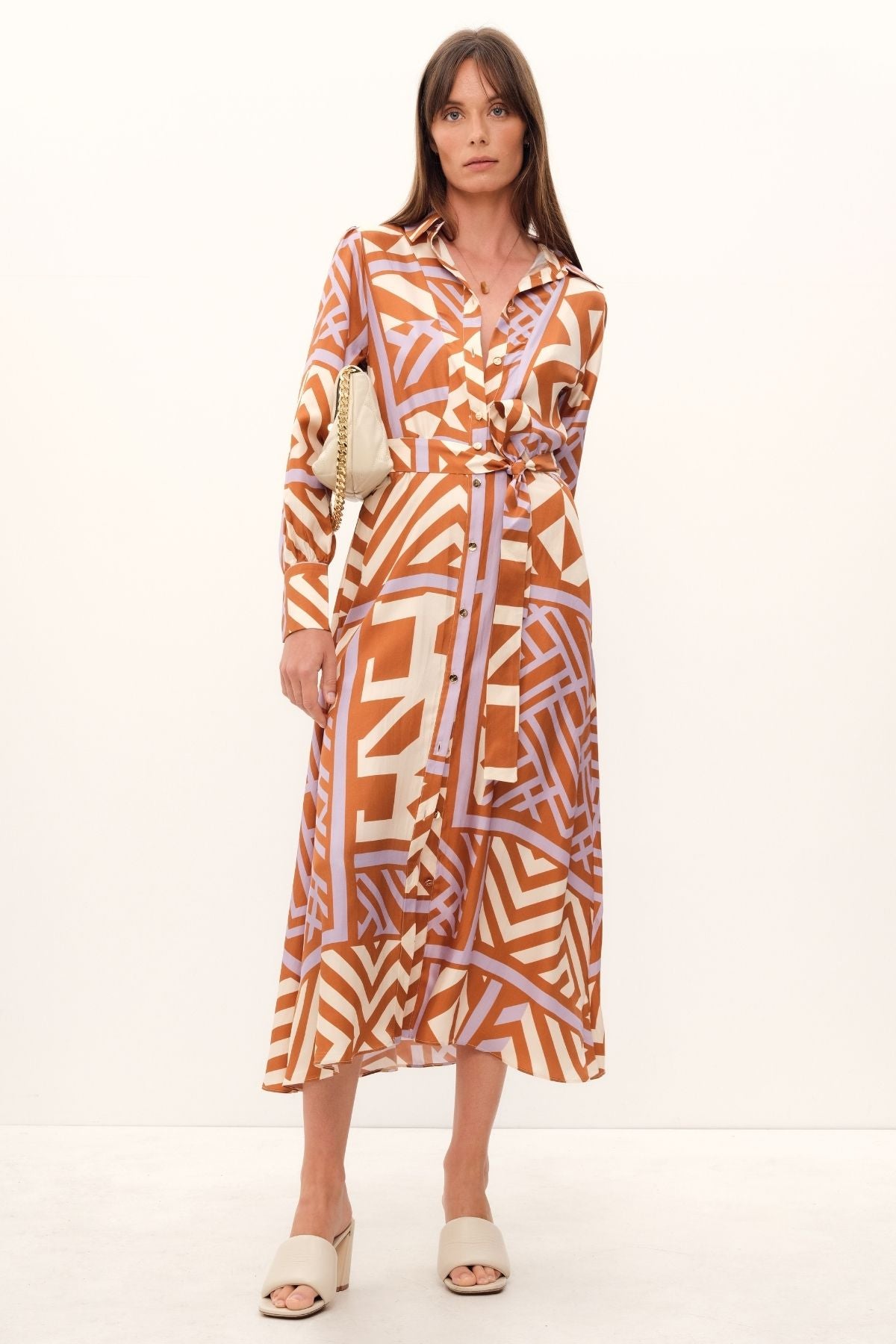 GINGER & SMARTS's House of Mirrors Shirt Dress is crafted from luxe silk twill and featuring a bold geometric print in crème, lilac, and tan, this classic dress is designed with front panel detailing, full length sleeves, and an optional waist tie.