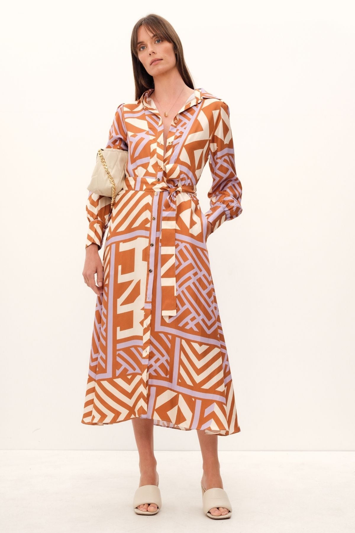 GINGER & SMARTS's House of Mirrors Shirt Dress is crafted from luxe silk twill and featuring a bold geometric print in crème, lilac, and tan, this classic dress is designed with front panel detailing, full length sleeves, and an optional waist tie.