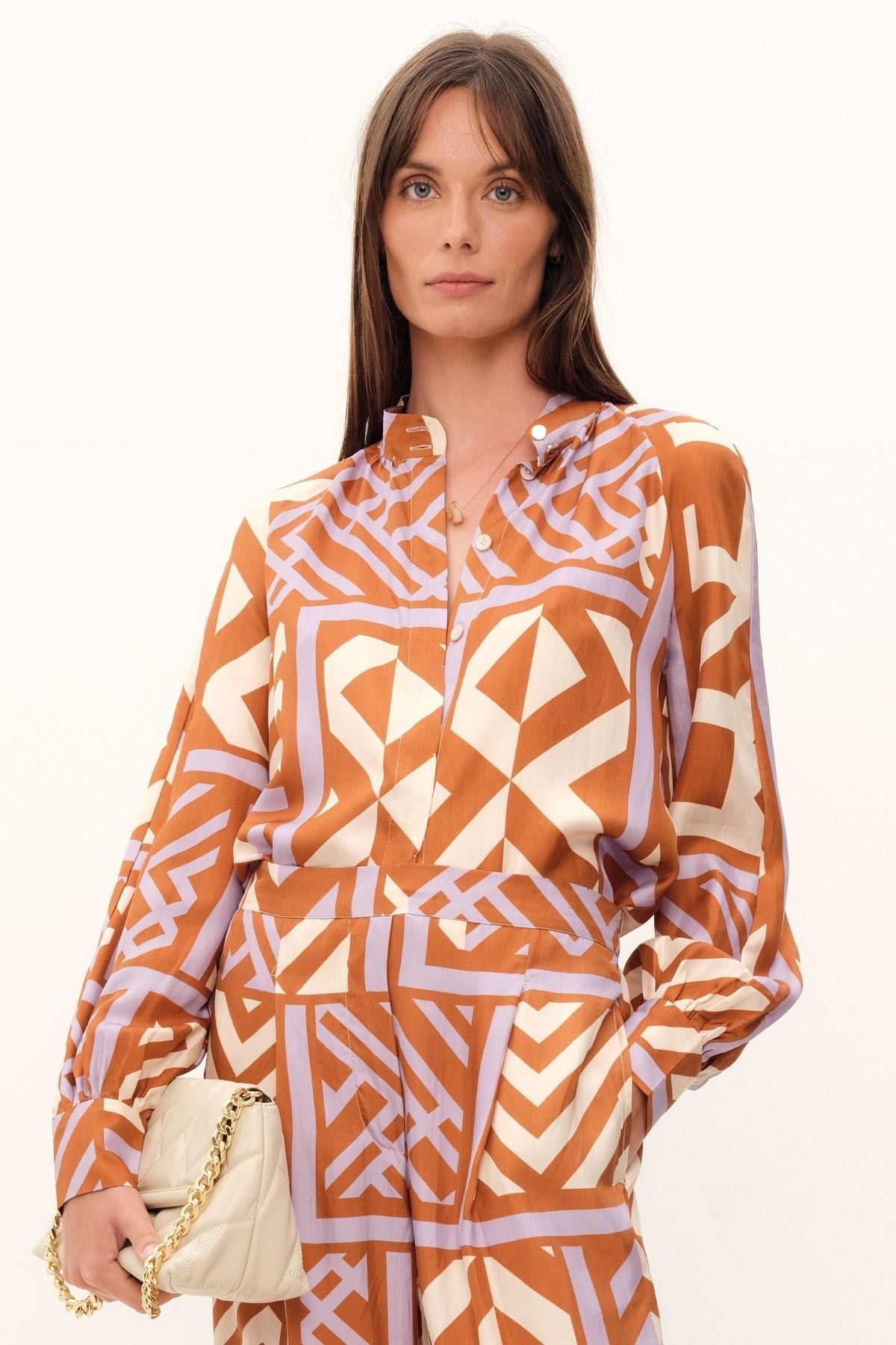 The House of Mirrors Blouse by GINGER & SMART has a bold geometric print in shades of crème, lilac, and tan. It includes a mandarin-style collar, concealed front placket, and full raglan sleeves with cuffs. Made with luxurious silk twill.