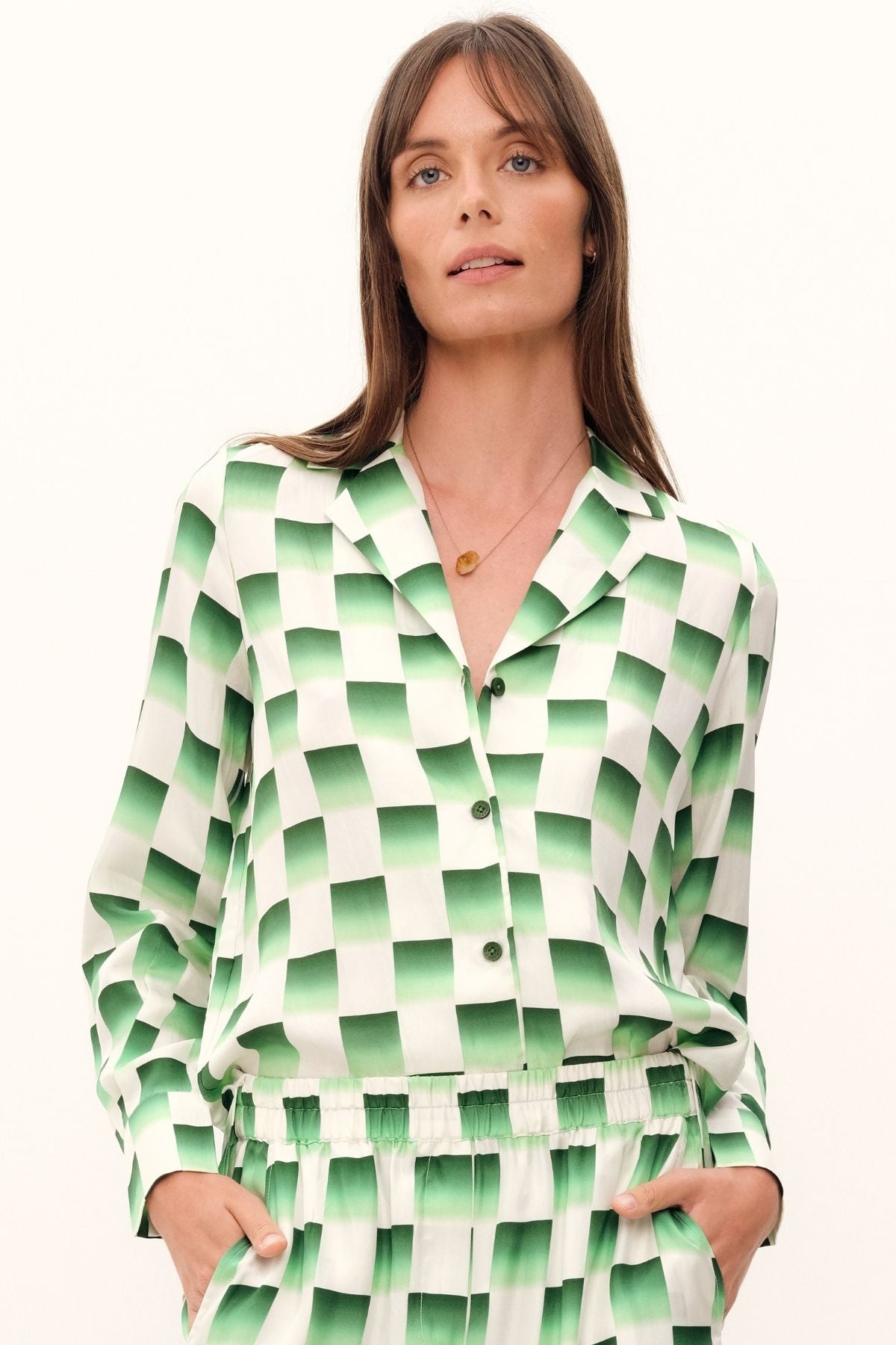 The Odyssey Blouse by GINGER & SMART is a luxurious silk twill with a checkerboard print in deep forest green and crisp white. It has a relaxed longline fit, straight hem, and GINGER & SMART logo Corozo nut buttons along the front.
