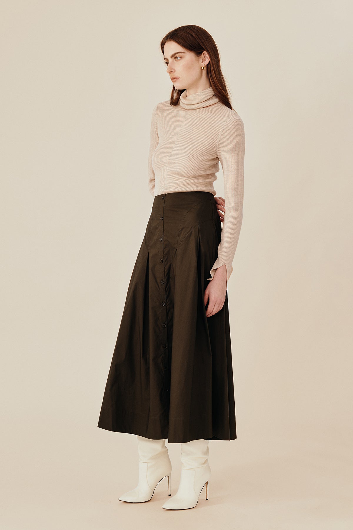 Model wearing Australian fashion designer GINGER & SMARTS midi Candor Skirt crafted in soft organic cotton featuring flattering panels on the hip with deep tucks that create a luxe wide hemline. Corozo buttons adorn the front opening. Worn with the women's Dimension Turtleneck Knit in oatmeal.