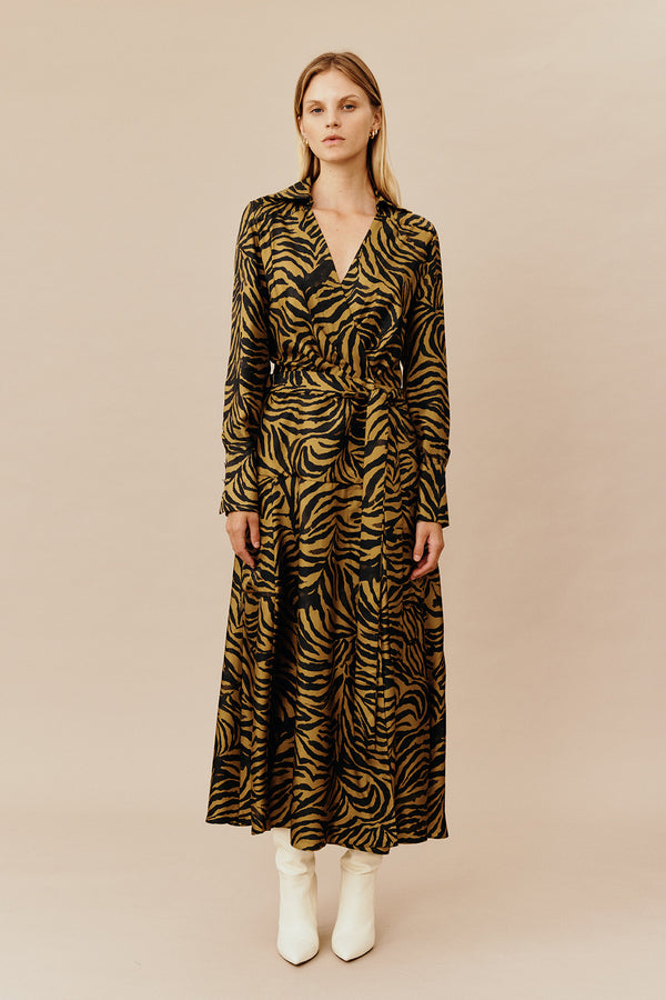 Model wearing Australian women’s fashion designer GINGER & SMARTS’ Feline Wrap Dress, crafted from a silk twill in olive green and gold animal print, featuring a sharp collar and gently flared skirt with a long shirt sleeve and metal logo buttons. 