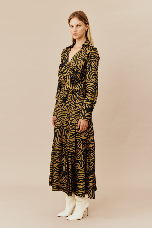 Model wearing Australian women’s fashion designer GINGER & SMARTS’ Feline Wrap Dress, crafted from a silk twill in olive green and gold animal print, featuring a sharp collar and gently flared skirt with a long shirt sleeve and metal logo buttons. 