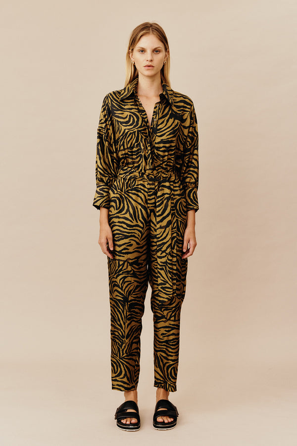 Model wearing Australian women’s fashion designer GINGER & SMARTS’ Feline Jumpsuit, crafted from a silk twill in olive green and gold animal print with a tapered leg silhouette, shirt collar, button through front, half sleeve and elasticised waist with tie. 