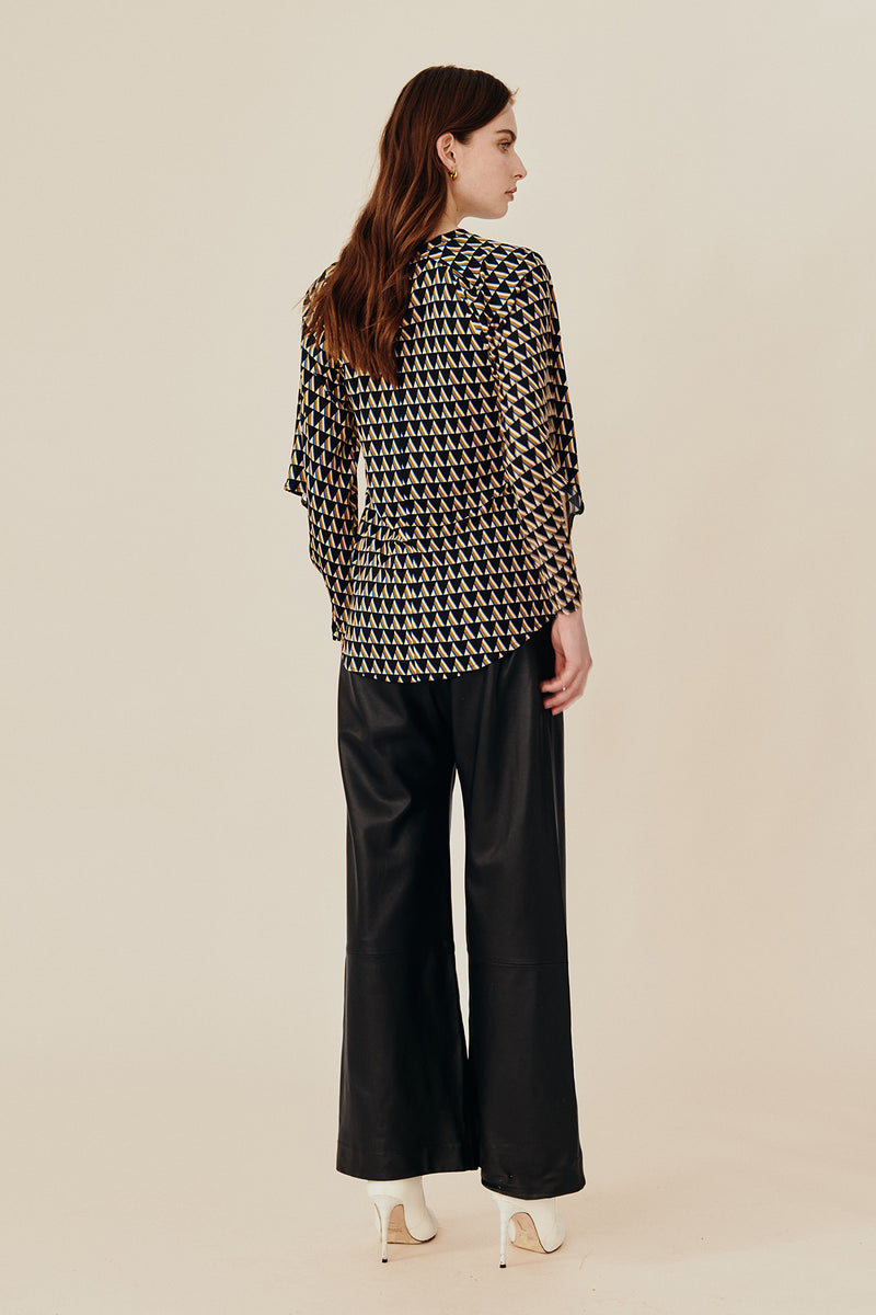 Back view of Australian luxury fashion designer GINGER & SMARTS' women's geometric printed silk long sleeve top with a crew neck and angular sleeve. Worn on a model with the women's black Genesis Leather Pant