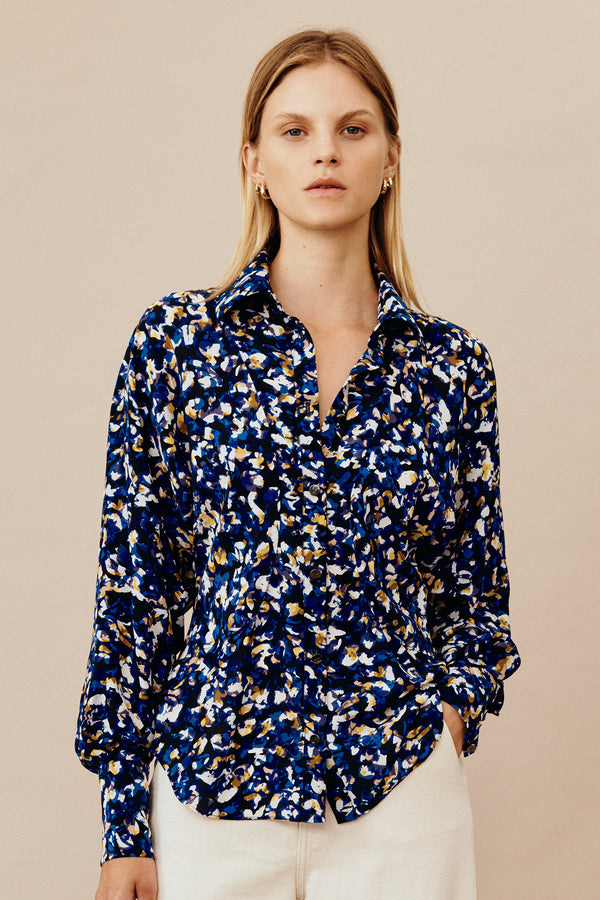 Model wearing Australian fashion designer GINGER & SMARTS' silk Terrazzo Blouse in blue with olivine, navy, and crème terrazzo print featuring a tailored fit with circular waist panels and a sharp collar with a generous sleeve and chic wide cuff.  