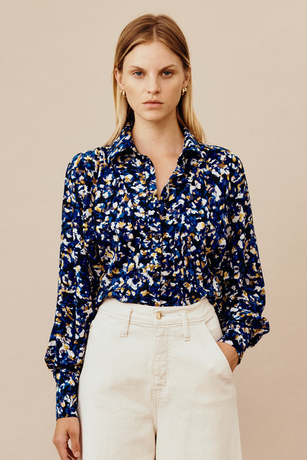 Model wearing Australian fashion designer GINGER & SMARTS' silk Terrazzo Blouse in blue with olivine, navy, and crème terrazzo print featuring a tailored fit with circular waist panels and a sharp collar with a generous sleeve and chic wide cuff.  