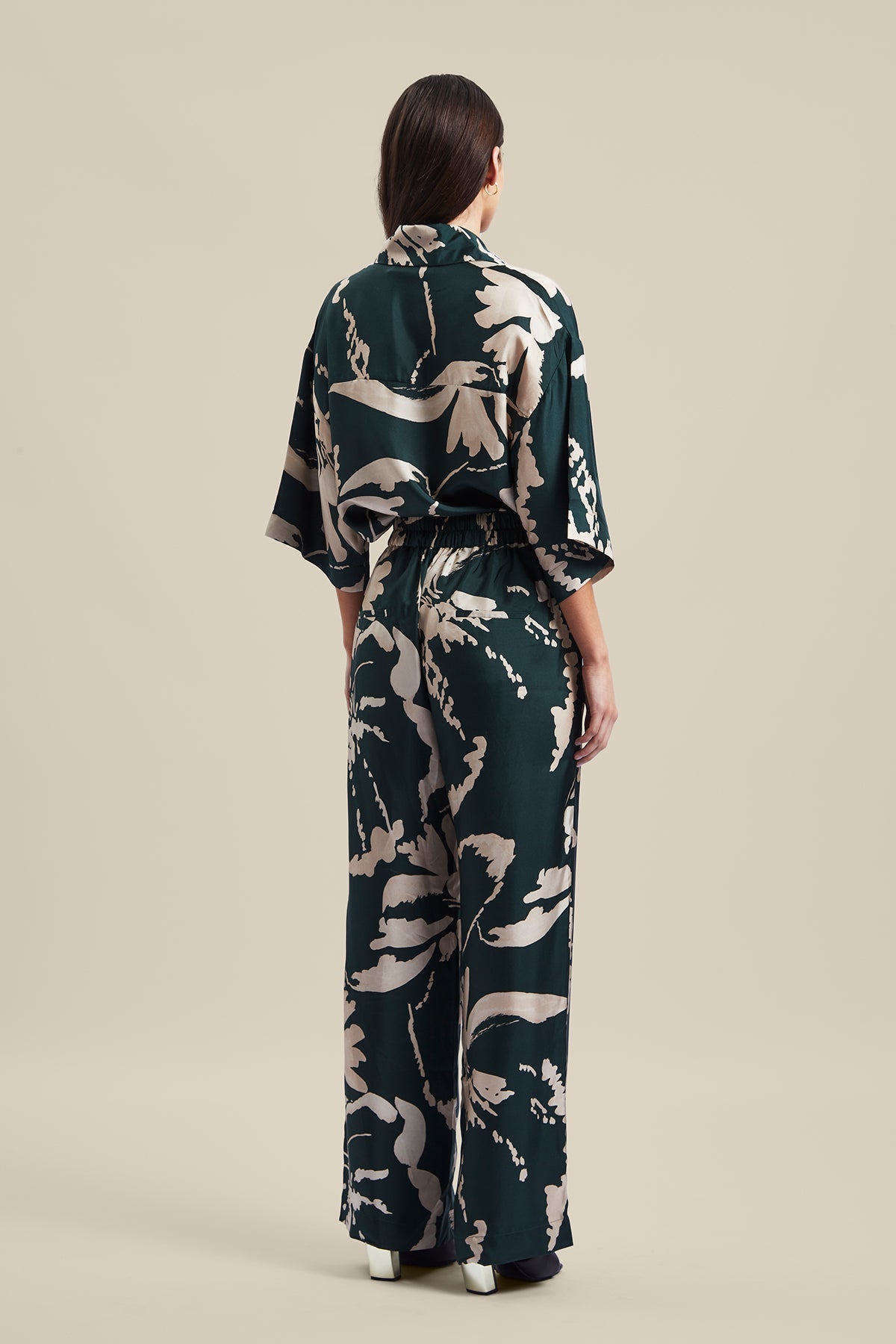 Back view of model wearing the Memoirs Pant from Australian Fashion Designer Ginger and Smart featuring is an abstract floral in green and crème with elastic waist and drawstring detail. Worn with the matching Memoirs Blouse.