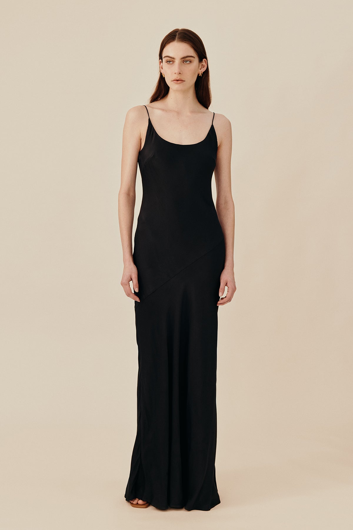 Model wearing 90’s inspired black Nocturnal Slip Dress from Australian luxury women’s designer GINGER & SMART, featuring body skimming fit, spaghetti straps, scoop neckline detail, maxi length, and a bias-cut skirt.