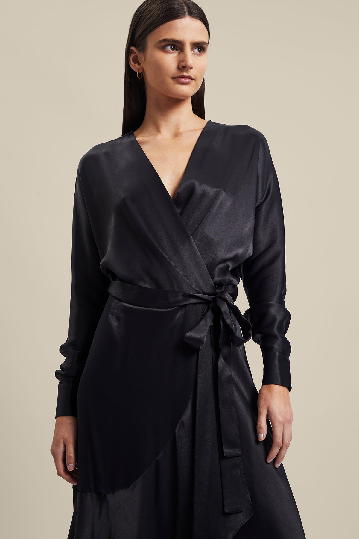 Model wearing black Nocturnal Wrap Dress from Australian luxury designer GINGER & SMART, featuring , long sleeves with wrist cuffs, waist tie, V neckline, midi length with bias cut asymmetrical hemline.